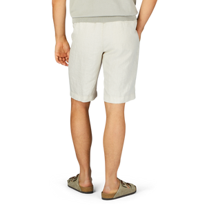 A person standing in Berwich cream beige washed linen drawstring shorts and casual shoes, viewed from the waist down.