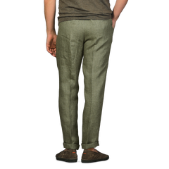 A person wearing Berwich's Green Linen Herringbone Drawstring Trousers in a slim fit and brown shoes stands with their back to the camera.