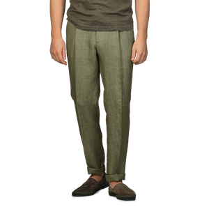 A person wearing Berwich's slim-fit Green Linen Herringbone Drawstring Trousers, a brown shirt, and brown shoes stands against a gray background, effortlessly blending style and comfort.