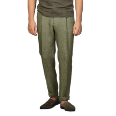 A person wearing Berwich's slim-fit Green Linen Herringbone Drawstring Trousers, a brown shirt, and brown shoes stands against a gray background, effortlessly blending style and comfort.