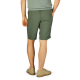 Person wearing Berwich militare green washed linen drawstring shorts and beige slip-on shoes standing with their back to the camera.
