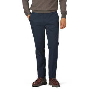 A person wearing a brown sweater, Navy Blue Cotton Twill Flat Front Trousers from Berwich, and brown shoes stands with their hands in their pockets against a plain background.