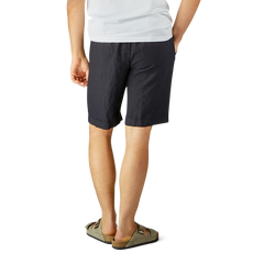 Man standing in Berwich navy blue washed linen drawstring shorts and a white t-shirt, wearing slip-on shoes, against a plain background.