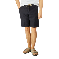 Man wearing Berwich navy blue washed linen drawstring shorts and gray sandals stands against a light background, focusing on his lower torso and legs.