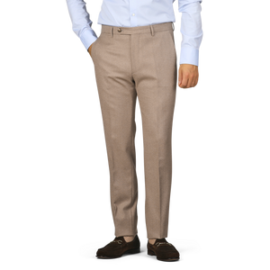 A person wearing Berwich's Oatmeal Melange Wool Flannel Flat Front Trousers, paired with a light blue shirt and brown loafers, stands casually with hands in pockets.