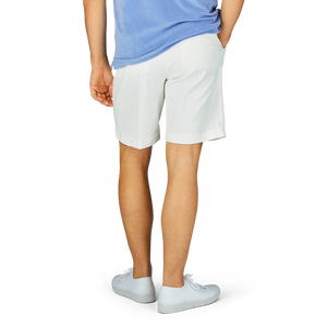 Man standing in Off-White Cotton Blend Pleated Shorts by Berwich and white sneakers, partial view from the side.