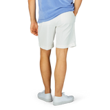 Man standing in Off-White Cotton Blend Pleated Shorts by Berwich and white sneakers, partial view from the side.