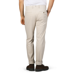 A person is wearing the Sand Beige Cotton Twill Flat Front Trousers from Berwich, paired with a white shirt in the Vulcano fit. They are standing with one hand in their pocket, facing away.