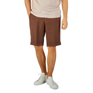 Man standing in Berwich terra brown washed linen drawstring shorts and white sneakers, cropped from the waist down.