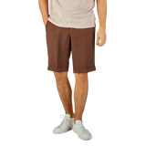 Man standing in Berwich terra brown washed linen drawstring shorts and white sneakers, cropped from the waist down.