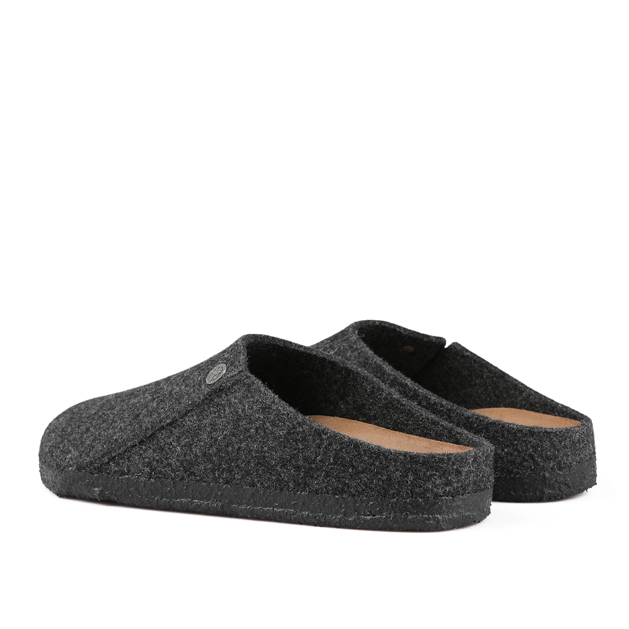 The Anthracite Grey Zermatt Rivet Slippers by Birkenstock are a pair of slippers crafted from dark gray wool felt with black soles, shown from a side angle, and include a removable footbed for enhanced comfort.