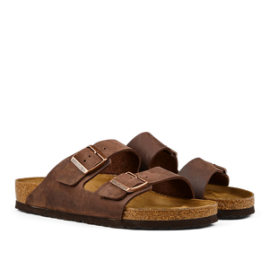 A pair of brown, Birkenstock Habana Brown Natural Leather Arizona sandals with adjustable leather straps and a cork footbed.