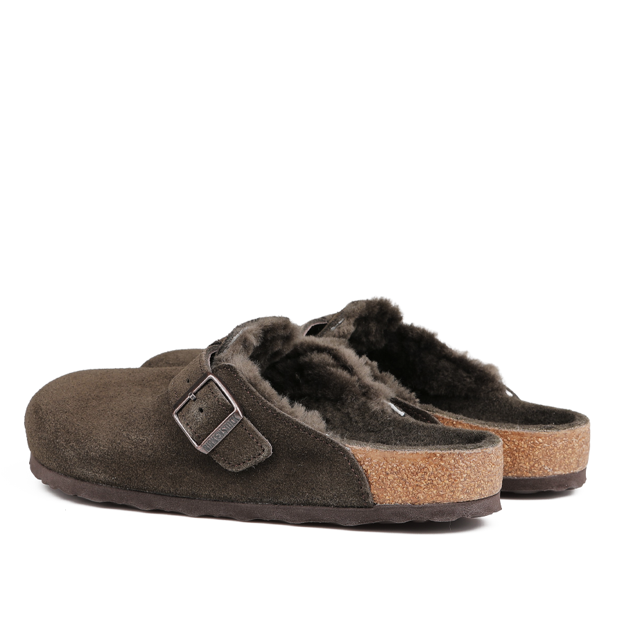 A pair of Mocca Brown Suede Shearling Lined Boston Slippers by Birkenstock, featuring a single buckle strap and cork soles for ultimate comfort.