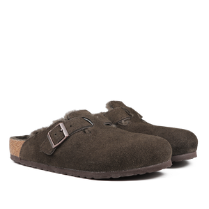 The Birkenstock Mocca Brown Suede Shearling Lined Boston Slippers are slip-on clogs with a buckle strap and cozy cork footbed, embodying the brand's famed comfort and style.