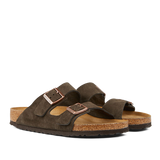 A pair of mocha brown suede leather Birkenstock Arizona sandals with cork soles on a transparent background.