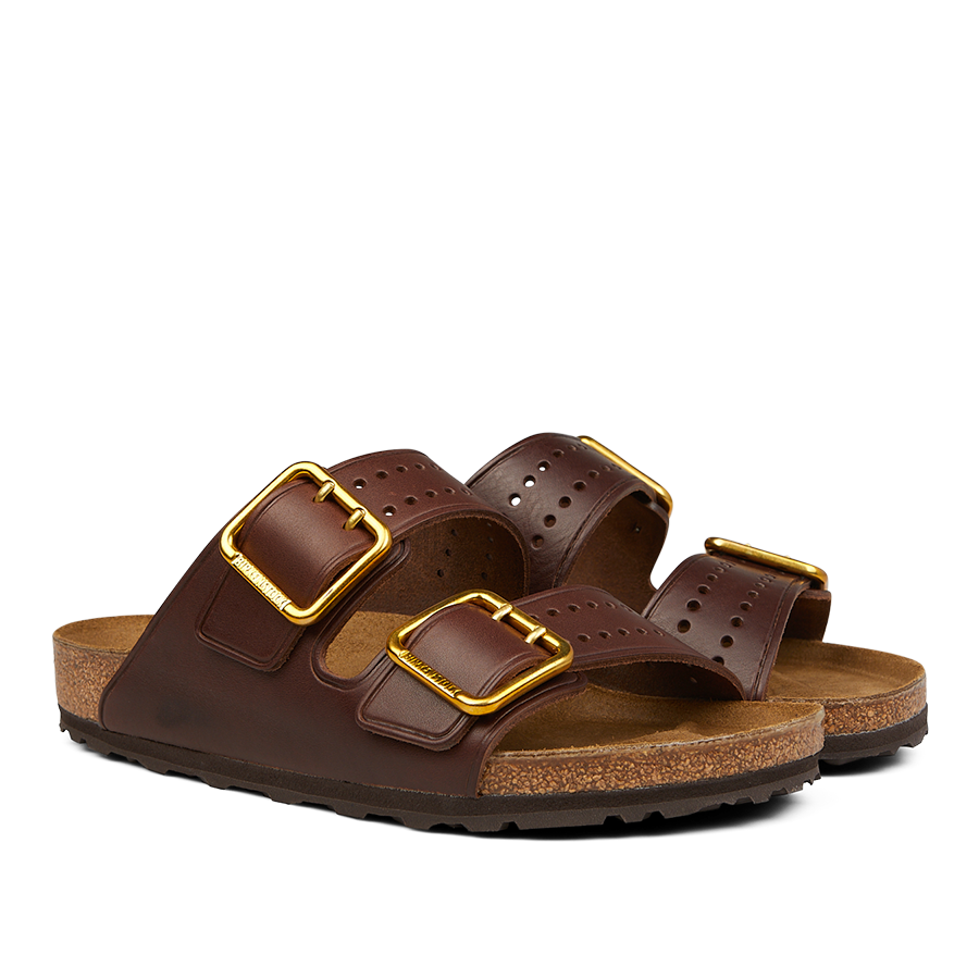 A pair of Birkenstock Roast Bold Natural Leather Arizona Sandals featuring two adjustable leather straps with gold buckles and a cork, anatomically-supported footbed.