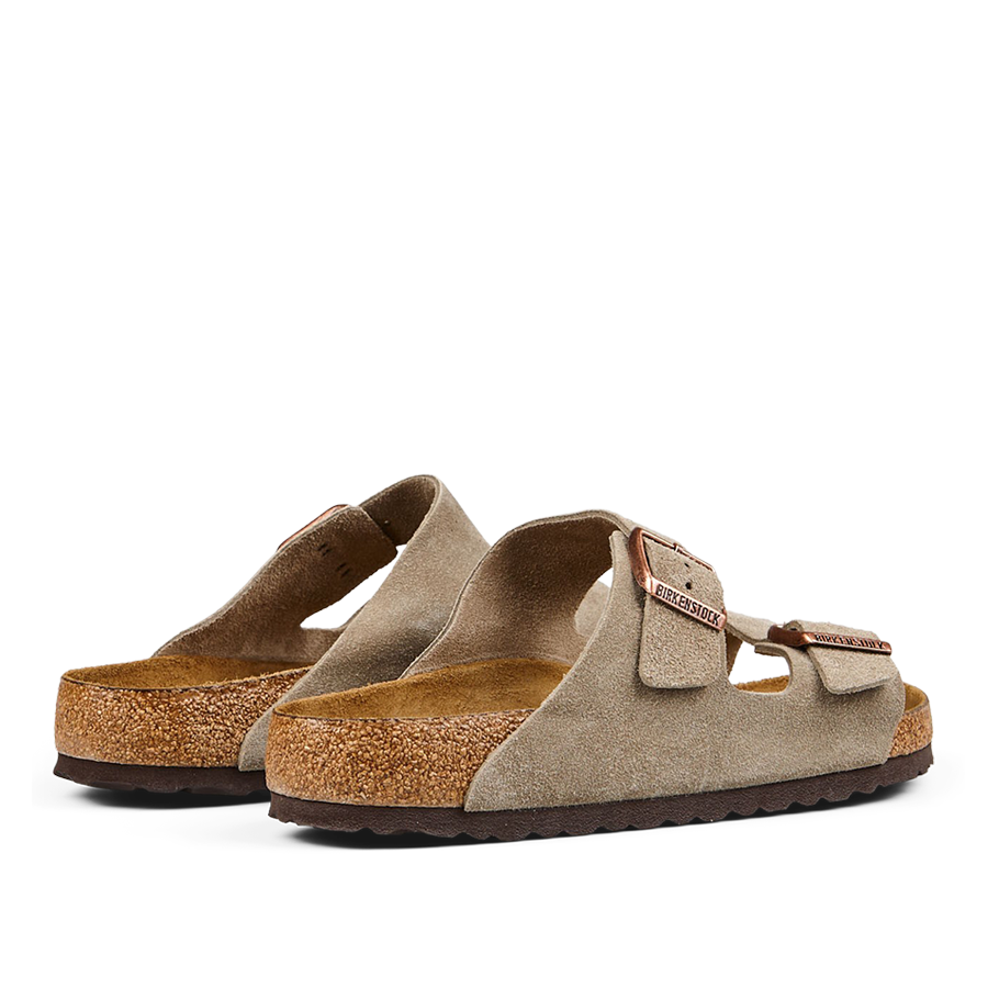 A pair of taupe beige suede leather Birkenstock Arizona sandals with adjustable straps and cork soles.