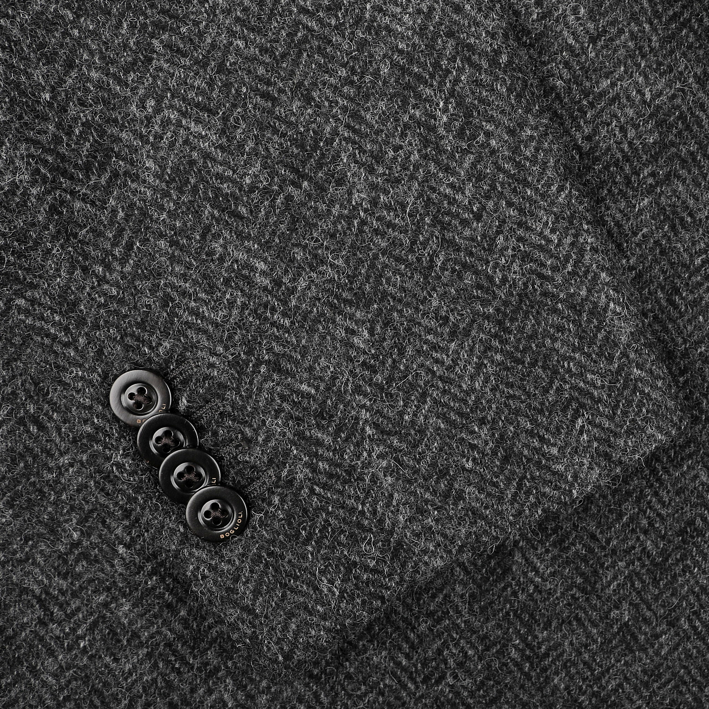 Close-up of the Dark Grey Herringbone Wool Tweed K Jacket by Boglioli, featuring an unstructured design with four black buttons accentuating its signature craftsmanship.