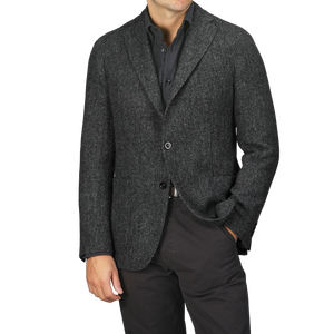 A person wearing a Boglioli Dark Grey Herringbone Wool Tweed K Jacket, featuring unstructured craftsmanship, over a button-up shirt, with one hand in their pants pocket.