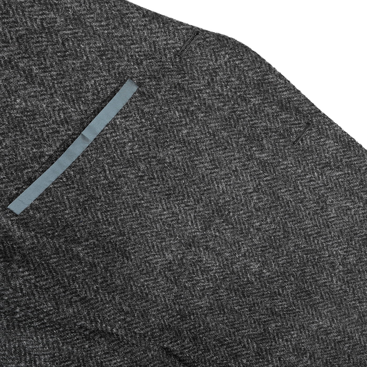 Close-up of a dark grey herringbone wool tweed K Jacket by Boglioli, highlighting the unstructured craftsmanship and a single horizontal pocket with a blue lining.