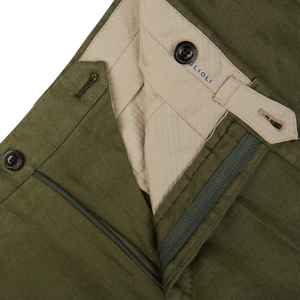 Close-up of an open olive green pair of Boglioli Green Washed Irish Linen Trousers with a zipper and a button, displaying the inner label and waistband construction.