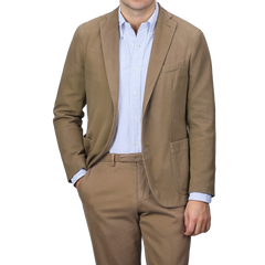 A person in a Boglioli Khaki Beige Heavy Cotton Twill Suit, paired with a blue and white striped shirt, stands with one hand in their pocket.