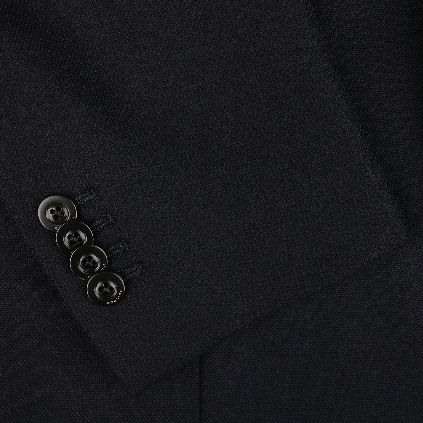 Close-up image of a navy blue jacket sleeve crafted from virgin wool by Boglioli, showcasing four black buttons neatly arranged in a row near the cuff.