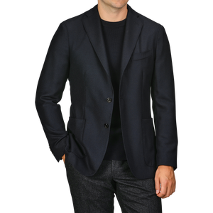 A person is seen wearing a Navy Blue Virgin Wool K Jacket by Boglioli over a black shirt, with their left hand in their trouser pocket. The trousers appear to be made of virgin wool and are grey. The person's head is not visible.