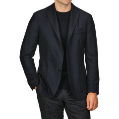 A person is seen wearing a Navy Blue Virgin Wool K Jacket by Boglioli over a black shirt, with their left hand in their trouser pocket. The trousers appear to be made of virgin wool and are grey. The person's head is not visible.