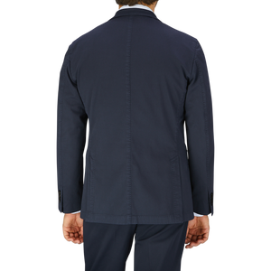 Rear view of a man wearing an unstructured dark blue Boglioli Navy Blue Washed Cotton K Jacket suit jacket and trousers, crafted in Italy, against a neutral background.
