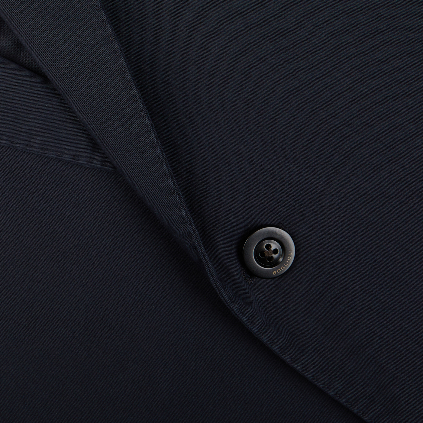 Close-up of a black button on dark fabric, likely a piece of Navy Blue Washed Cotton K Jacket crafted by Boglioli in Italy.