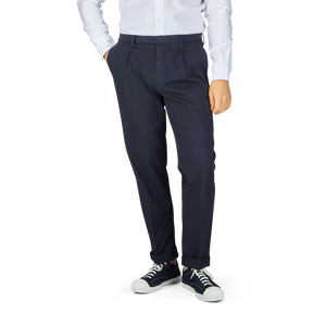 A person standing wearing Boglioli navy blue washed cotton pleated trousers and a white shirt with black and white sneakers.