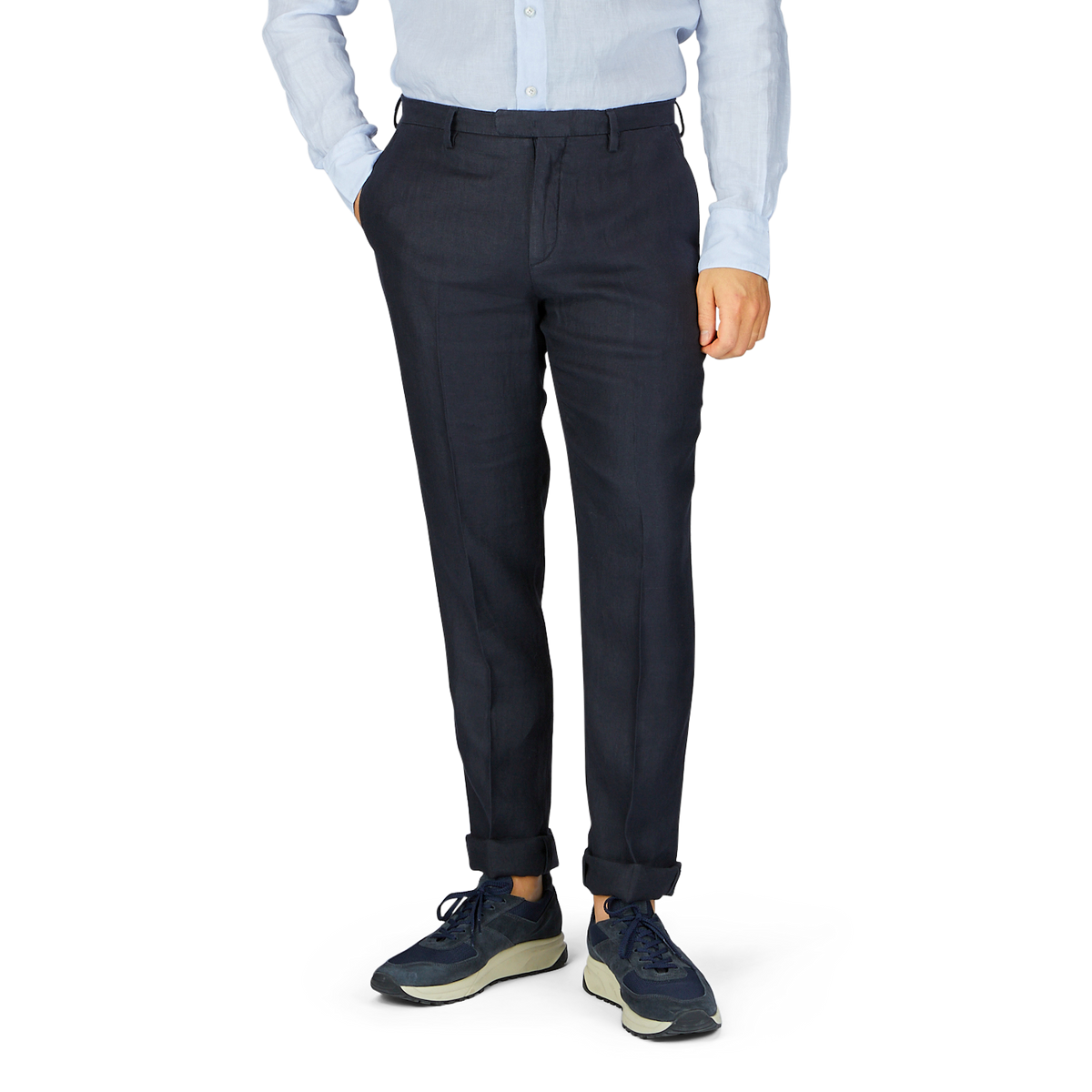 Man wearing a light blue, pure linen shirt, Boglioli navy blue washed Irish linen trousers, and sneakers, standing against a neutral background.