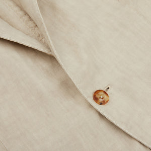 A close up of a button on a beige jacket made with linen fabric, complementing the Boglioli Sand Beige Washed Linen Unstructured Suit.