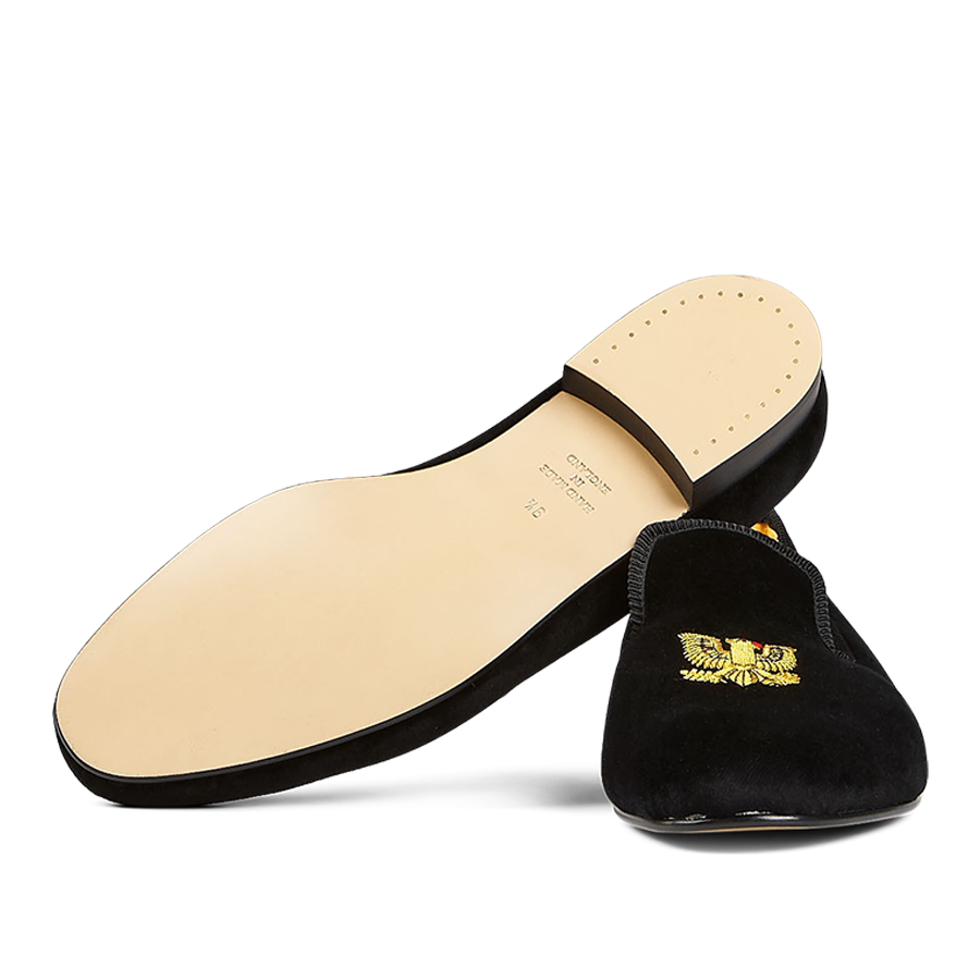 A single Black Velvet American Eagle slipper from Bowhill Elliott with a gold embroidered emblem on the upper, displayed against a translucent striped background.