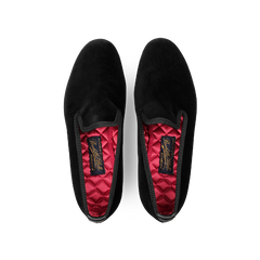 A pair of Plain Black Velvet Albert Slippers by Bowhill Elliott, featuring a luxurious red quilted inner lining and a branded insole logo, designed for style and comfort, viewed from above.