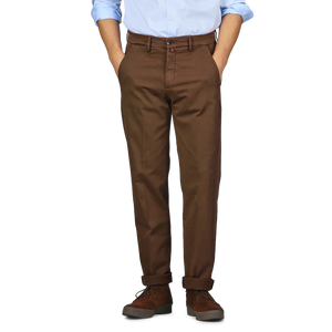 A person in a light blue shirt and Briglia's Brown Cotton Stretch Soho Trousers stands against a plain background with their hands in their pockets. They are wearing dark brown shoes with a thick sole.