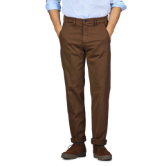 A person in a light blue shirt and Briglia's Brown Cotton Stretch Soho Trousers stands against a plain background with their hands in their pockets. They are wearing dark brown shoes with a thick sole.