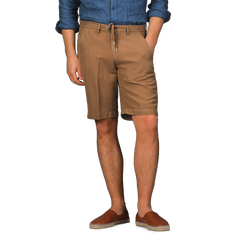 A person in a blue shirt, Camel Brown Cotton Linen Drawstring Malibu Shorts by Briglia, and brown loafers stands against a gray background.