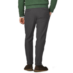 A person wearing Briglia's Dark Grey Cotton Twill BG21 Pleated Trousers and a green sweater, complemented by brown shoes, stands with hands in pockets, facing away.