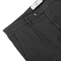 Close-up of Briglia's Dark Grey Cotton Twill BG21 Pleated Trousers, featuring a black button and belt loops, with vertical stitching adorning the waistband and a brand label inside. Crafted by an Italian trouser specialist, these pants are made from pure cotton twill for a refined touch.