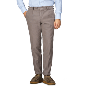 Person wearing Mole Brown Cotton BG21 Pleated Trousers by Briglia and brown shoes, with hands in pockets, against a gray background.