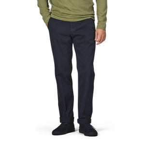 A person in a green long-sleeve top, Briglia's Navy Blue Cotton Stretch Soho Trousers, and black shoes stands against a plain background with hands in pockets.