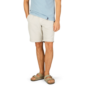 Man wearing a light blue t-shirt, Briglia Stone Beige Cotton Linen Pleated Shorts with an adjustable waistband, and sandals.