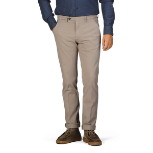 A person wearing Briglia Taupe Beige Cotton Stretch BG62 Trousers, a blue long-sleeve shirt, and brown shoes stands with their hands in their pockets.