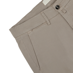 Close-up of Briglia's Taupe Beige Cotton Stretch Soho Trousers featuring a button and zipper fly, belt loops, and front pockets, lying flat against a gray background.