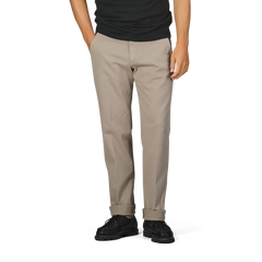 A person wearing Briglia Taupe Beige Cotton Stretch Soho Trousers, a black shirt, and black shoes stands with hands in pockets against a plain background.