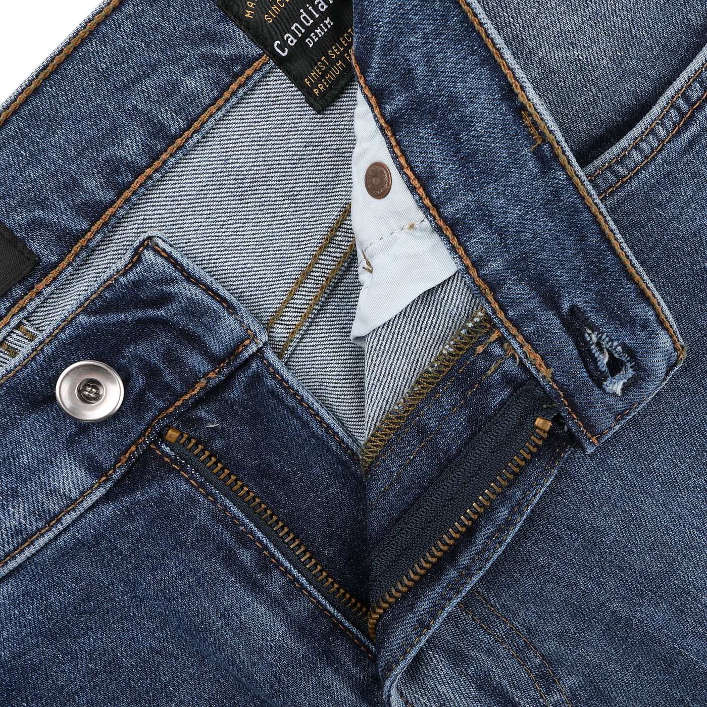 Close-up of C.O.F Studio's Indigo Blue Washed Organic Cotton M8 Jeans, showcasing a partially open zipper and metal button. Tags and stitching details emphasize the craftsmanship of the organic Kuroki Selvedge denim.