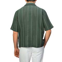 A person is seen from the back wearing a C.O.F Studio Dark Green Striped Crochet Relaxed Camp Shirt with white pants.