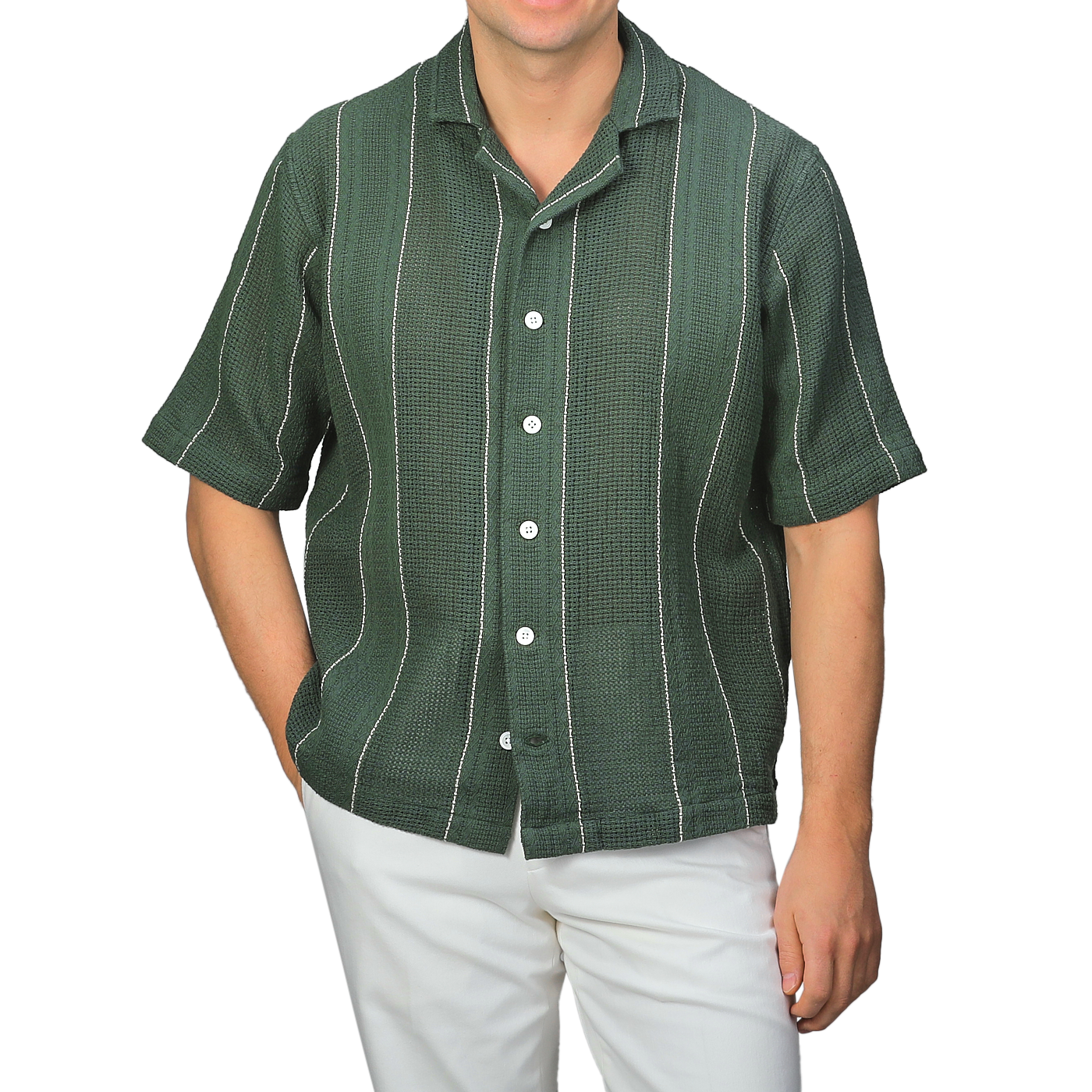 A person stands against a neutral background wearing C.O.F Studio's Dark Green Striped Crochet Relaxed Camp Shirt paired with white pants.